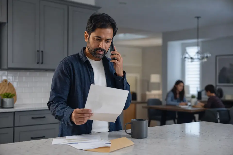 Man on the phone reading an opened letter at a kitchen island