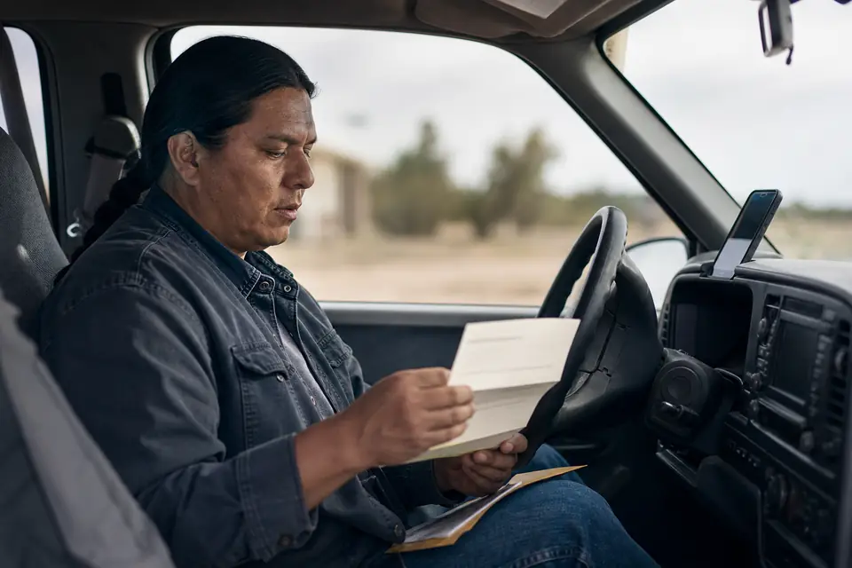 Man in a parked pickup truck reading an opened letter with a phone nearby