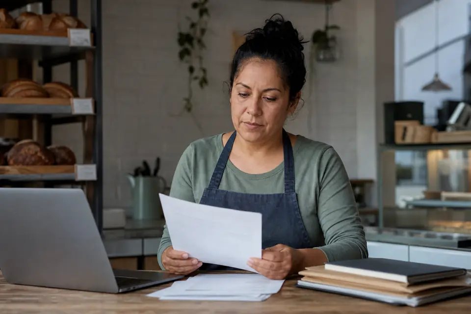 Bakery owner reviewing a printed letter at the back counter of her shop